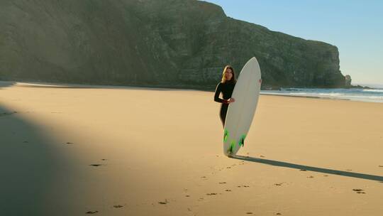 女孩拿着冲浪板站在沙滩上