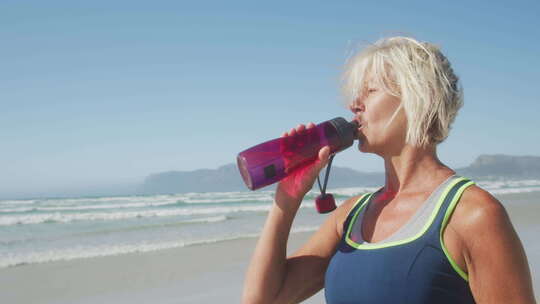 在海滩上喝水的运动妇女