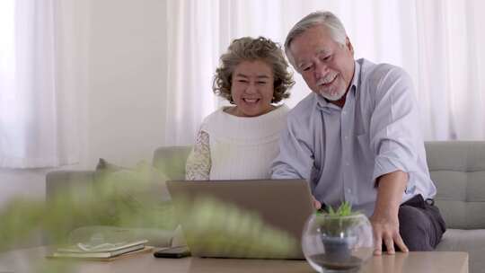 一对亚洲老年人在线视频会议，客厅里有笔记本电脑。