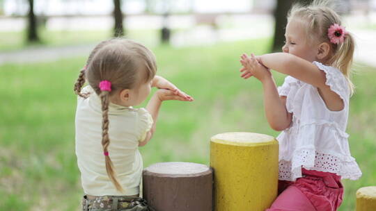 两个小女孩坐在草地的木墩上玩耍
