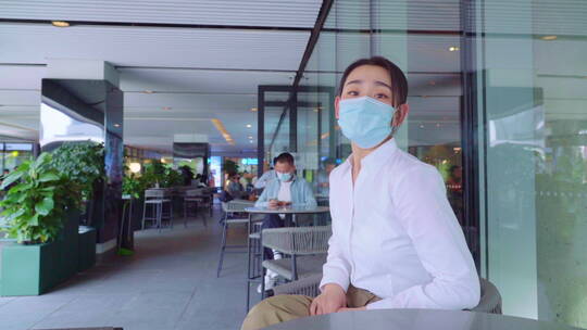 青年女人戴着口罩坐在咖啡馆里视频素材模板下载