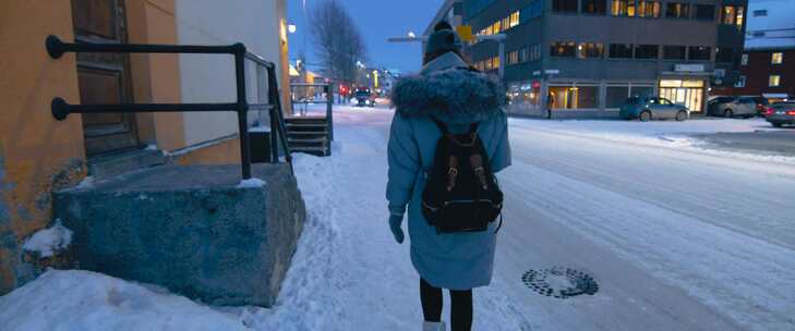 穿着冬装的女人在白雪皑皑的大街上靠近建筑