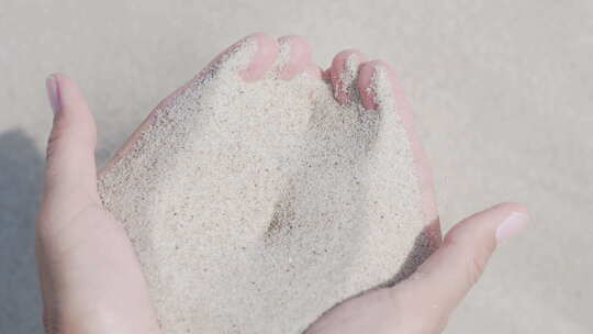 沙子从手指间倾泻而出。女人在沙滩上玩沙子。时间的象征。