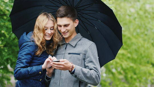 年轻夫妇打着伞玩手机视频素材模板下载