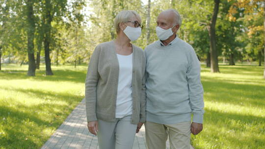 戴着医用口罩在公园散步的快乐老年夫妇在户外享受夏日