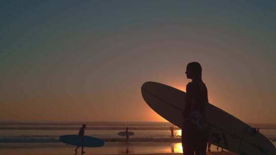 海边夕阳下女孩拿着冲浪板等朋友