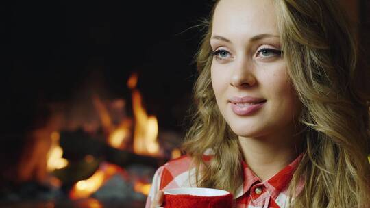 年轻女人在燃烧的壁炉旁喝茶