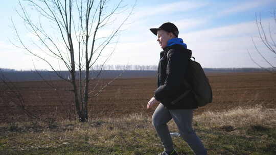 早春，戴着帽子的小男孩在犁地附近慢跑，穿视频素材模板下载