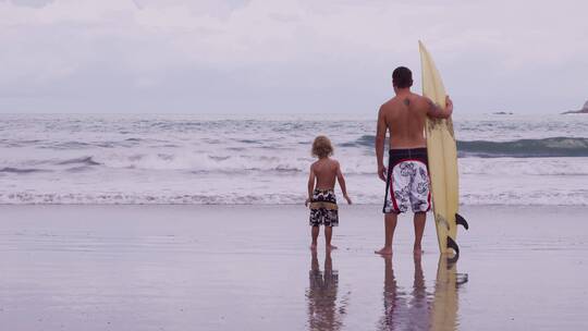 父亲拿着冲浪板和儿子站在海边