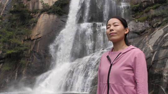 亚洲中国人女性在瀑布下张开双臂拥抱自然