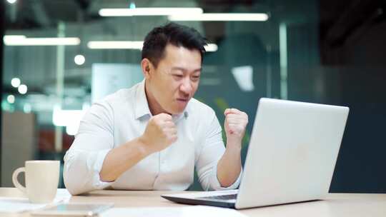 兴奋的亚洲商人在办公室看着笔记本电脑屏幕