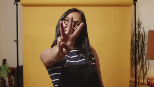 年轻微笑的亚洲女人在黄色背景的家庭工作室里竖起大拇指倒数3,2,1视频素材模板下载