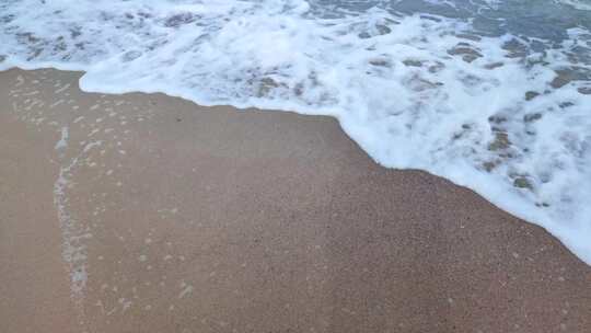 海边沙滩上白色泡沫滚动的海浪特写镜头