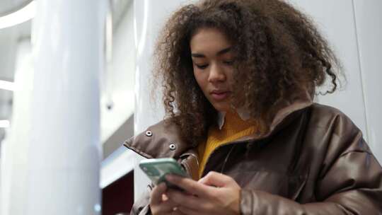 专注的深色皮肤女性在地铁里等火车，并使用智能手机上网