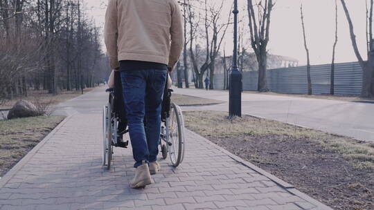 男人推着轮椅上的朋友散步视频素材模板下载