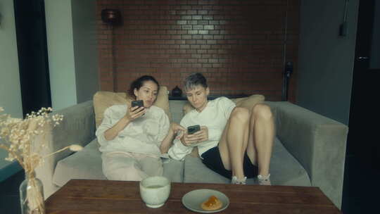 两个年轻女人拿着手机坐在家里的沙发上
