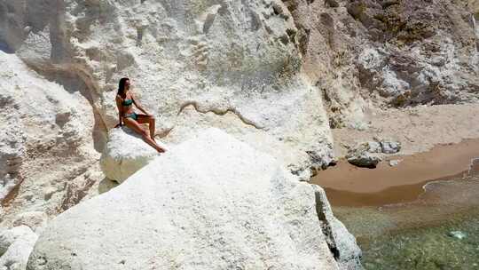 穿比基尼女性坐在海边岩石上