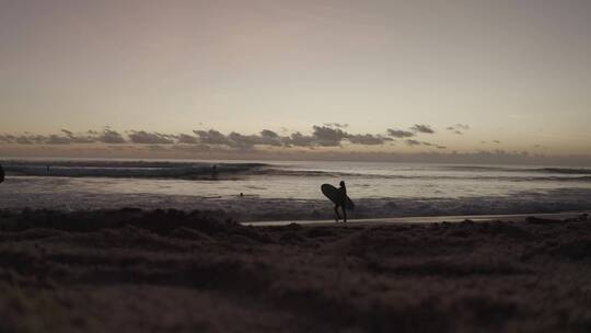 日落时女人在海边拿着冲浪板走