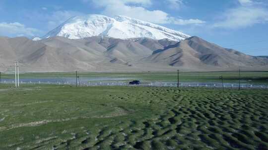 4k航拍汽车行驶在新疆慕士塔格峰下牧场旁
