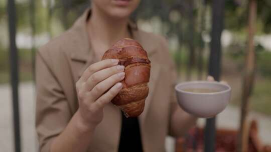 手握羊角面包和茶杯在户外露台上吃早餐的特