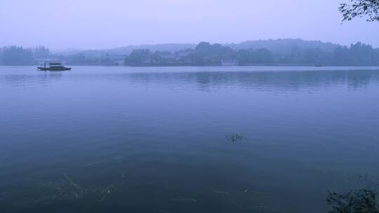 一艘渔船划在黄昏时烟雾迷蒙的杭州西湖上