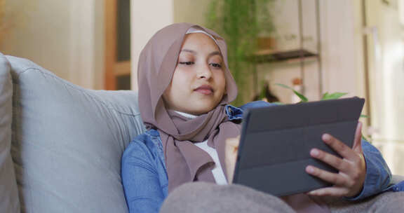 戴头巾的女人在沙发上使用平板电脑