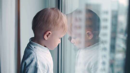 童年在封锁期间一个在家隔离的小男孩看着窗外自我隔离