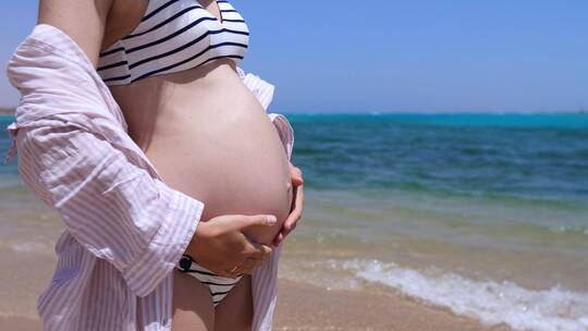 怀孕的性感女子站在海滩上摸自己的肚子