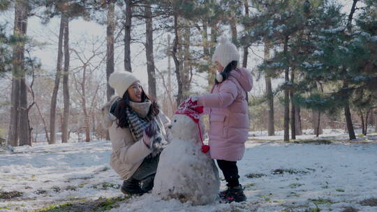 年轻妈妈和女儿在雪地里堆雪人