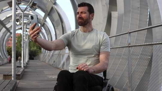 坐在轮椅上的快乐男人在城市大桥上进行视频
