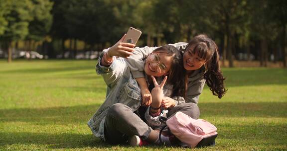 两位可爱女学生在大学校园草地上用手机自拍