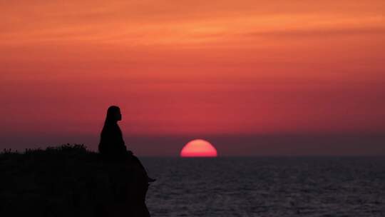孤独的女生坐在悬崖海边看夕阳