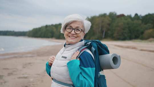 肖像微笑的老年灰发女人旅行者戴着眼镜背着