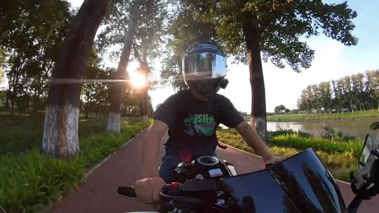 夕阳落日夏天男子骑摩托车在林荫大道