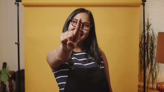 年轻微笑的亚洲女人在黄色背景的家庭工作室里竖起大拇指倒数3,2,1