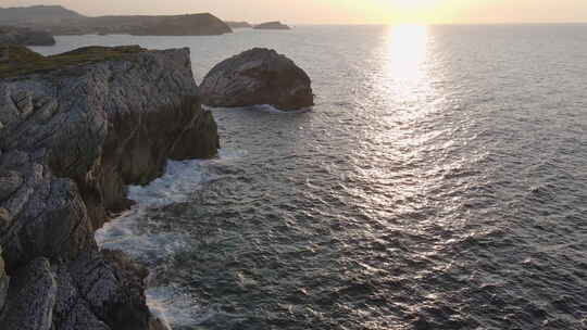 鸟瞰日落时海浪拍打在海岸的岩石上