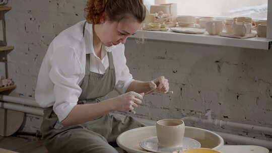 一个女人坐在陶器轮子上制作一个陶瓷碗