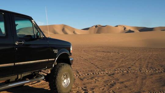 平移镜头的两辆车停在沙漠的沙丘和山脉