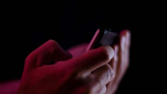 当视频在黑暗的房间侧面特写中播放时，拇指在智能手机上