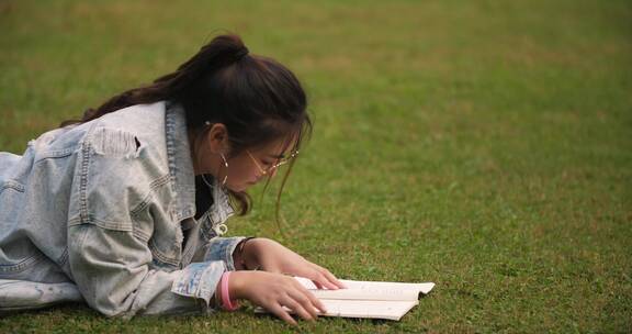 大学校园里女学生趴在草地上看书学习休闲