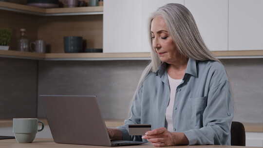 老年女士买家祖母购物者成熟女性坐在厨房支付笔记本电脑使用的公用事业账单