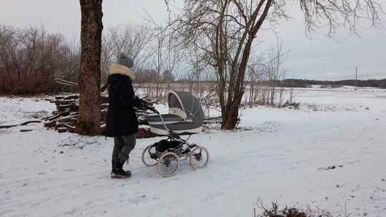 女母亲推着婴儿车慢慢走在白雪皑皑的乡间小