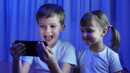孩子们兄弟姐妹在黑暗中对着手机摄像头嬉笑