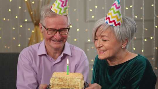 许愿家庭戴派对帽的老年夫妇在家一起庆祝生