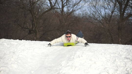 男人趴在滑雪毡上从雪山上滑下来