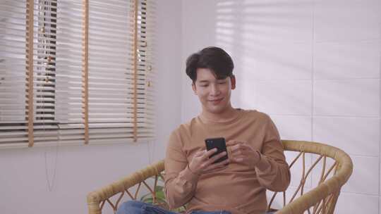 在他的客厅里，一名亚洲男子正在打电话，用智能手机听和交谈。视频素材模板下载