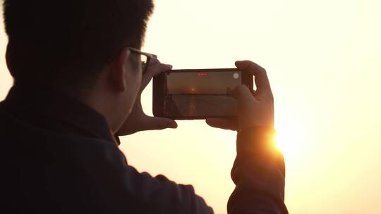 男人用手机拍摄海上日落美景