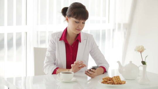 年轻女子坐在桌旁喝茶和使用手机
