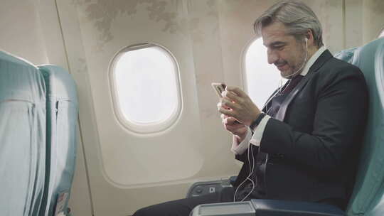 商人在飞行期间在飞机座位上使用手机浏览互联网