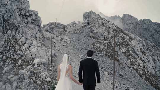 新婚夫妇手牵手走向云雾笼罩的阿尔卑斯山山顶